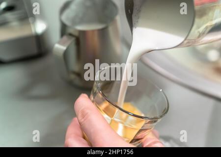 Il barista versa la schiuma di latte in un bicchiere per espresso. Foto Stock