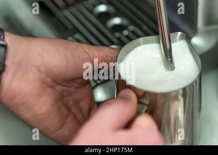 Un uomo sbatte il latte per un latte in una caraffa di acciaio. Foto Stock