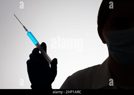 Silhouette di un medico con siringa riempita di liquido blu. Concetto di vaccinazione. Foto Stock