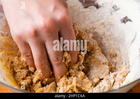 Primo piano delle mani del panettiere della donna impastando l'impasto nel recipiente di miscelazione. Pasticceria fatta in casa per torte o biscotti. Foto Stock