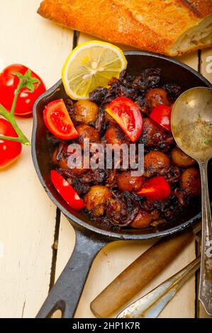 Baby seppie arrostite in padella di ferro con pomodori e cipolle su tavola in legno rustico Foto Stock