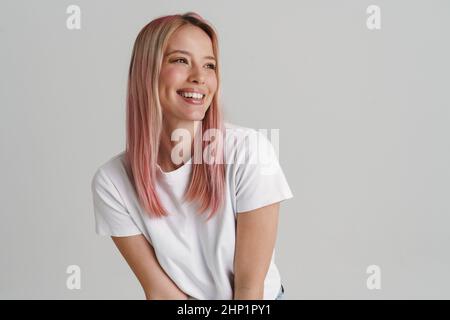 Felice sorridente giovane donna bianca bionda in abiti casual in piedi su sfondo grigio parete, guardando da parte Foto Stock