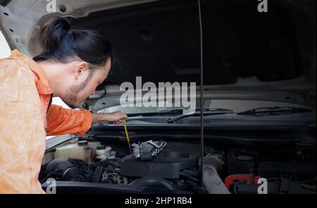 Il meccanico in uniforme arancione ha aperto il cofano e scoperto un'anomalia che impedisce l'avviamento della vettura. Il concetto di soluzioni fuori sede Foto Stock