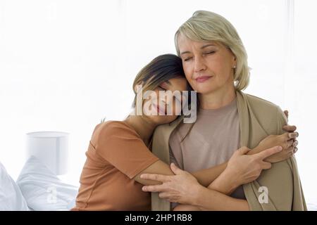 Happy mix pelle famiglia vivere insieme, figlia asiatica e adottato cuddle madre caucasica a vicenda con sorrisi. Concetto di amore e di condivisione del tempo Foto Stock