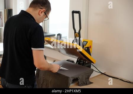 Occhiali uomo-operaio indietro utilizzando calore termico tessuto applicazione di trasferimento pressa. Tecnologia di stampa abbigliamento art design Foto Stock