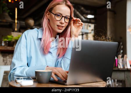 Giovane donna che indossa occhiali che lavora con un computer portatile mentre si siede in un bar Foto Stock