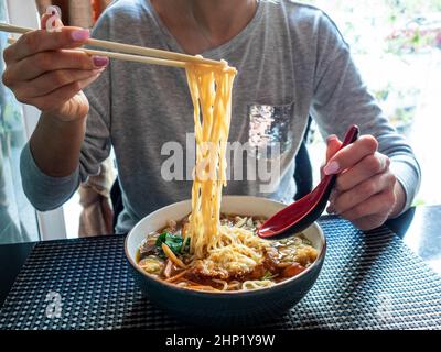 Concetto: Cibo asiatico sano. Donna irriconoscibile che sta per mangiare. Tenere tagliatelle di ramen giapponesi con bacchette. Foto Stock