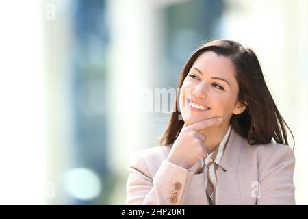 Donna d'affari felice che pensa guardando il lato all'aperto nella strada Foto Stock