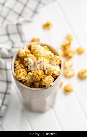 Popcorn caramello dolce in tazza su tavola bianca. Foto Stock