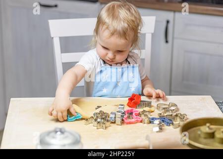 Adorabile simpatico ragazzo biondo taglia l'impasto nella cucina domestica. Orizzontalmente. Foto Stock