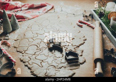 Buon Natale, Felice Anno Nuovo. Biscotti di pan di zenzero che cucinano, pasta arrotolata sul tavolo, forme di taglio differenti, stella, cuore, animali. Famiglia festosa Foto Stock