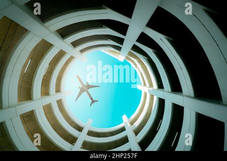 Edificio con vista dal basso e parcheggio auto a più piani con aereo che vola sopra l'edificio. Logistica dell'aria. Aviazione e viaggi d'affari. Architettura della curva a spirale Foto Stock