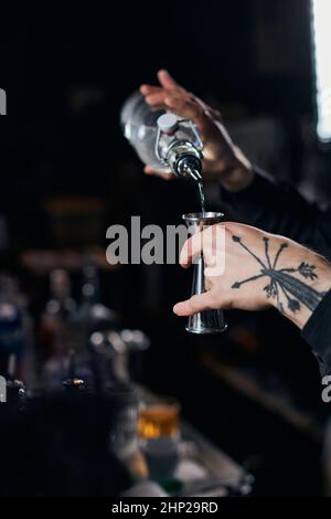 Il barman in grembiule aggiunge l'ingrediente al bicchiere da cocktail Foto Stock