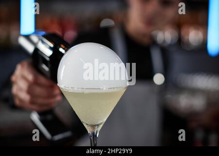 il barman sta sorseggiando un cocktail con una bolla d'aria fumosa al bar, primo piano Foto Stock