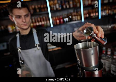 Barman in grembiule aggiunge l'ingrediente allo shaker dal jigger Foto Stock