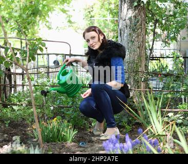 Donna vestita casual positiva in giardino acque fiori Foto Stock