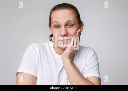 carino timido giovane uomo bello in t-shirt isolato su sfondo grigio. Emozioni umane, espressioni facciali Foto Stock