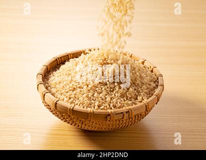 Il riso marrone momento è versato in un colander di bambù messo su un fondo di legno. Foto Stock