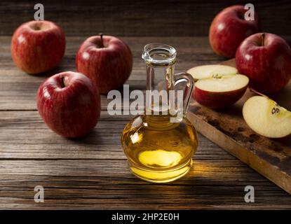 Aceto di mele in un contenitore di vetro su un fondo di legno con un sacco di mele intorno. Foto Stock