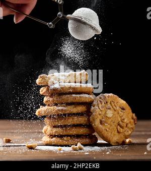 una pila di biscotti rotondi al forno cosparsi di zucchero in polvere su un tavolo di legno, sfondo nero Foto Stock