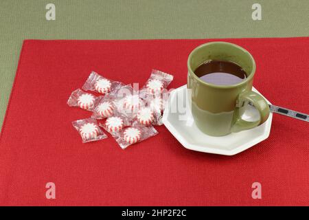 Bevanda calda a base di cioccolata di un mix natalizio servito in una tazza di caffè verde vicino alla caramella alla menta piperita su un placemat rosso su una tovaglia verde. Cioccolata calda Foto Stock