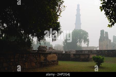 Qutb Minar la mattina di nebbia visto da all'interno di terreni storici e rovine fiancheggiate da alberi a Delhi, Inida. Foto Stock