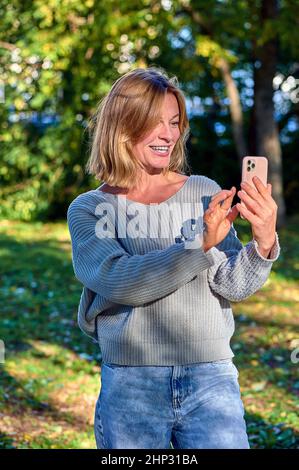 Una donna in un parco in estate parla durante una videochiamata al telefono. Foto di alta qualità Foto Stock