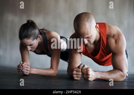 Spingi la tua strada verso il fitness. Shot di un uomo e di una donna che fanno esercizi di asse in palestra. Foto Stock