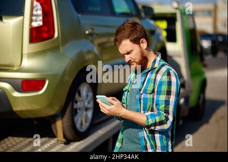 Uomo che chiama il telefono all'agente assicurativo mentre traina il camion che raccoglie la sua auto rotta dopo un incidente stradale Foto Stock