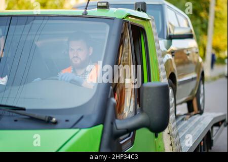 Uomo che guida un camion di traino con auto. Servizio di evacuazione rapido. Primo piano immagine ritagliata. Messa a fuoco selettiva Foto Stock