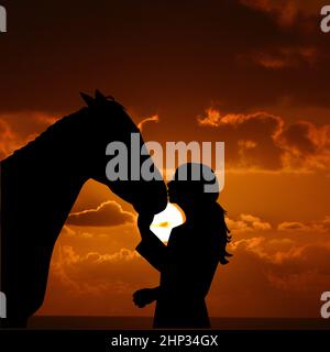 Silhouette di una giovane ragazza con cavallo che gli dà un bacio all'alba Foto Stock