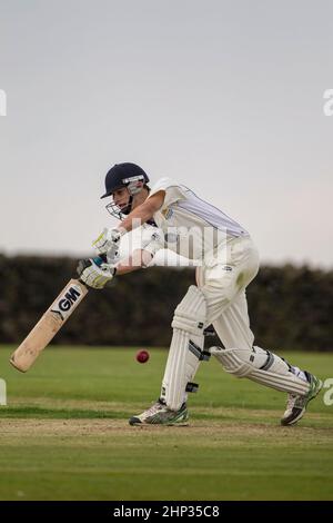 Primo piano di un battitore di cricket che gioca in avanti per una consegna e che guida la palla al di fuori del campo durante una partita di cricket villaggio. Foto Stock