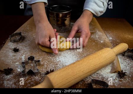 In primo piano vi è una tavola con la pergamena da forno, sulla quale si trova l'impasto che le mani del cuoco si sbriciolano, una spina di laminazione, la cuocina da forno Foto Stock