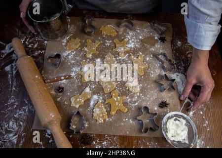 Ci sono biscotti pronti di varie forme sulla pergamena da forno, una spina di laminazione, tagliatubi e un setaccio con farina, farina i. Foto Stock