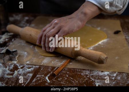 L'impasto viene arrotolato con un matterello su pergamena, la farina viene sparsa, la foto è in una chiave scura. Foto di alta qualità Foto Stock