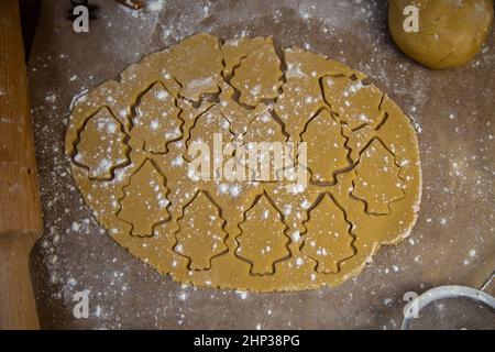 Nello strato di pasta arrotolato, molti alberi di Natale sono tagliati, che sono contrassegnati con contorni, l'impasto si trova su forno pergamena, accanto ad esso giace Foto Stock