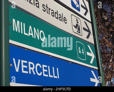 Indicazioni per Milano e Vercelli nel nord Italia. Cartello della polizia metropolitana parzialmente visibile. Foto Stock