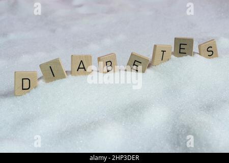 Le lettere su piccoli tasselli di legno che formano la parola diabete su una distesa di zucchero Foto Stock