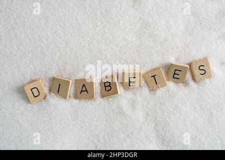 Le lettere su piccoli tasselli di legno che formano la parola diabete su una distesa di zucchero Foto Stock