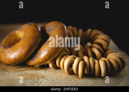 pannolino a forma di anello decorato con semi di papavero e un mazzo di bagel giace su carta pergamena, sfondo di legno Foto Stock