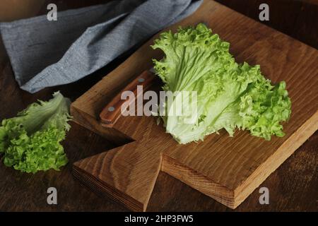 Concetto di alimentazione sana. Lattuga biologica verde cruda pronta a tritare sul tagliere con coltello. Foto Stock