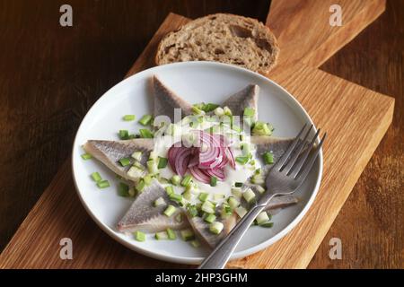 Filetti di aringhe con salsa di crema con cetrioli, cipolla rossa e spezie sul taglio di tavola di legno . Foto Stock