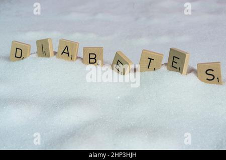 Le lettere su piccoli tasselli di legno che formano la parola diabete su una distesa di zucchero Foto Stock