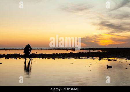 Silhouette del fotografo che guarda al mirino sulla fotocamera per catturare il tramonto in serata alla spiaggia di Pakarang, Phang Nga, Thailandia Foto Stock