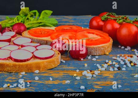 Spalmare il burro sul pane con pomodori a fette e ravanelli. Spuntino fresco su sfondo di legno naturale. Foto Stock