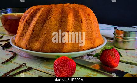 Torta di sabbia in vecchio stile con una tazza di tè nero e pezzi di vaniglia su sfondo di legno. Pan di Spagna al tuorlo d'uovo con fragole su fondo bianco rustico Foto Stock