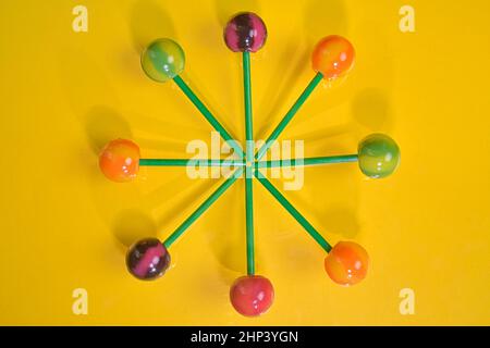 Gustosi lecca lecca su sfondo giallo pastello. Set di lollipop colorati realistici su bastoncini di plastica verdi. Estate e pop art. Vista dall'alto. Foto Stock