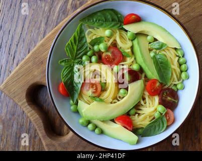 Insalata di pasta con piselli verdi, avocado, pomodori ciliegini e basilico su rustico fondo di legno. Vista dall'alto. Foto Stock