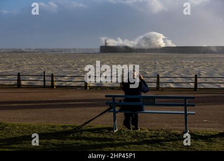 Newhaven Lighthouse, Regno Unito, 18th febbraio 2022. Un membro del pubblico siede e guarda le onde che colpiscono il Muro del mare del Faro di Newhaven nel pomeriggio mentre la tempesta Eunice penetra la costa meridionale dell'Inghilterra nel Sussex occidentale. Credit: Steven Paston/Alamy Live News Foto Stock