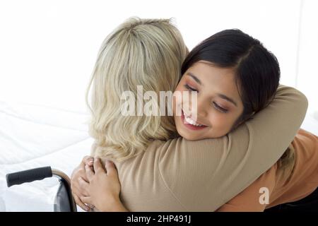 Happy mix pelle famiglia che vivono insieme, figlia asiatica coccola capelli biondo madre con sorrisi. Primo piano Foto Stock